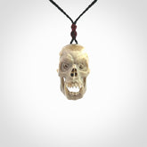 This picture shows a medium sized Deer Antler Bone skull pendant that we have hand carved. It is polished to a soft shine and is a very striking piece. The cord is a black colour and has a small burgundy floret binding just above the pendant.